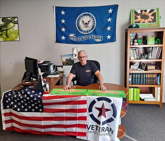 Navy Veteran, Veteran Owned Small Business, Veterans Day - image of man sitting at desk with American flag